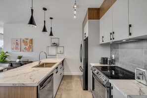A modern kitchen with a marble countertop, stainless steel appliances, pendant lighting, and a built-in oven.