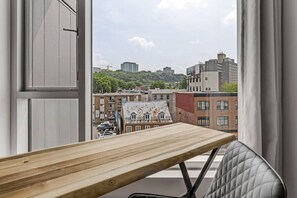 Ein Zimmer mit Holztisch und Blick auf eine Stadtlandschaft durch ein Fenster.