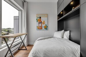 A bedroom with a bed, a window with a view, a table, and a wall with a poster. - Cozy & Co | Le Spritz | Centre-ville + Parking (Québec City)