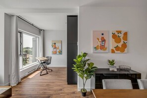 Ein modernes Wohnzimmer mit großem Fenster, einem Essbereich mit Tisch und Stühlen sowie Kunstwerken an der Wand.