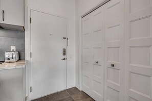 A hallway with a white door, a built-in shelf with a toaster, and a tiled floor.
