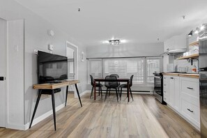 Eine moderne Küche mit Essbereich, einem Fernseher und einem großen Fenster mit Jalousien.