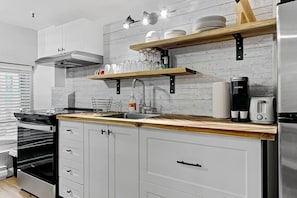 Eine moderne Küche mit einem Edelstahl-Kühlschrank, einem eingebauten Backofen, einer Spüle und Holzregalen über der Arbeitsplatte.