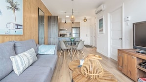 A modern living room with a sofa, a dining area with chairs, a wooden coffee table, and a television on a wooden cabinet. - Cozy & Co | The GH View | Centre-ville + Parking (Québec City)