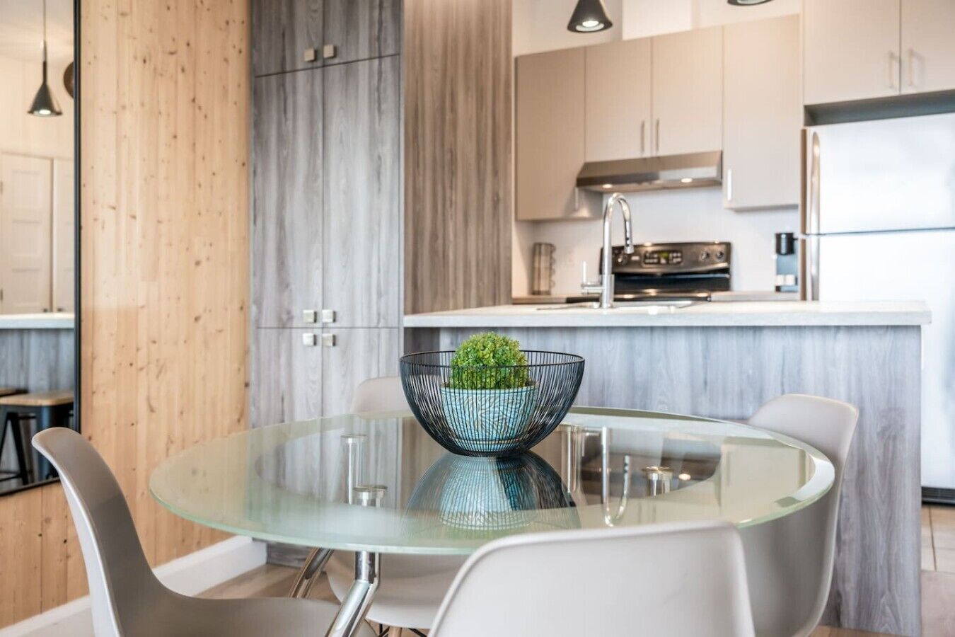Une cuisine moderne dotée d’un îlot central, d’appareils électroménagers en acier inoxydable et d’une table à manger en verre, assortie de chaises.