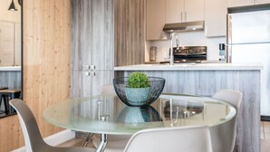 A modern kitchen with a central island, stainless steel appliances, and a glass dining table with chairs. - Cozy & Co | The GH View | Centre-ville + Parking (Québec City)
