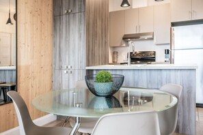 Une cuisine moderne dotée d’un îlot central, d’appareils électroménagers en acier inoxydable et d’une table à manger en verre, assortie de chaises.