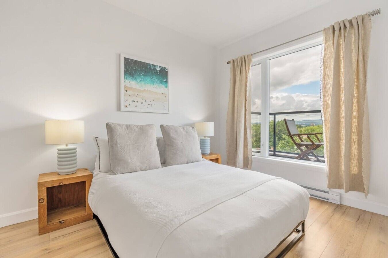 Une chambre avec un grand lit, deux tables de chevet avec des lampes, une fenêtre avec des rideaux et une vue sur la plage.