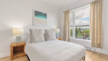 Une chambre avec un grand lit, deux tables de chevet avec des lampes, une fenêtre avec des rideaux et une vue sur la plage.