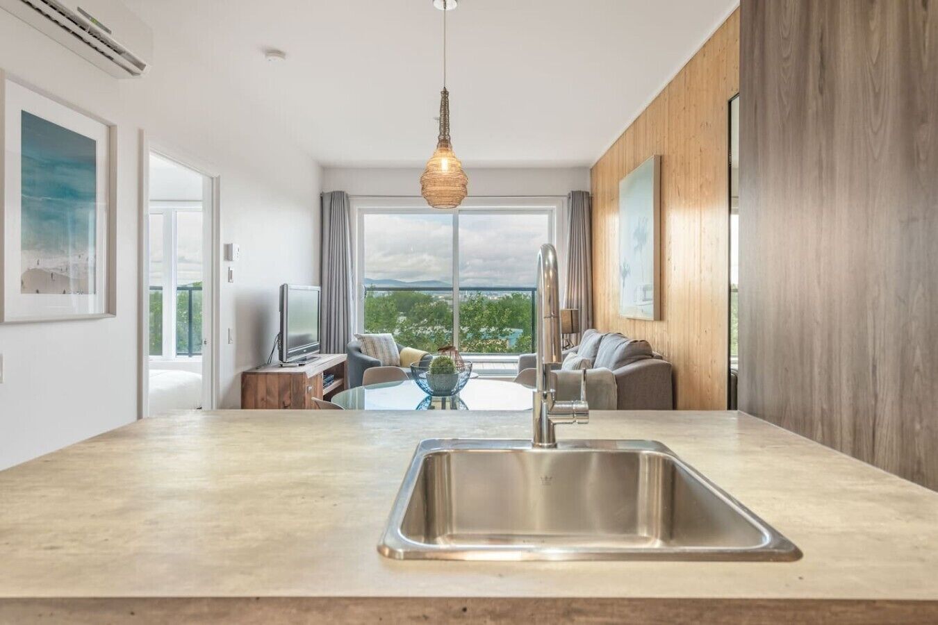 A modern kitchen with a large island, stainless steel sink, and a hanging light fixture.