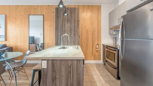 A modern kitchen with a central island, stainless steel appliances, and wooden paneling. - Cozy & Co | The GH View | Centre-ville + Parking (Québec City)
