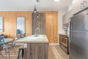 Une cuisine moderne dotée d’un îlot central, d’appareils électroménagers en acier inoxydable et de panneaux muraux en bois.
