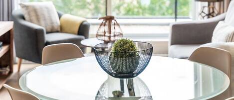 Un moderno salón con una mesa de vidrio, un cuenco metálico con una planta y vistas a zonas verdes.