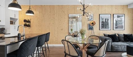 Een moderne keuken met een centraal eiland, zwarte stoelen, een glazen eettafel en hanglampen.