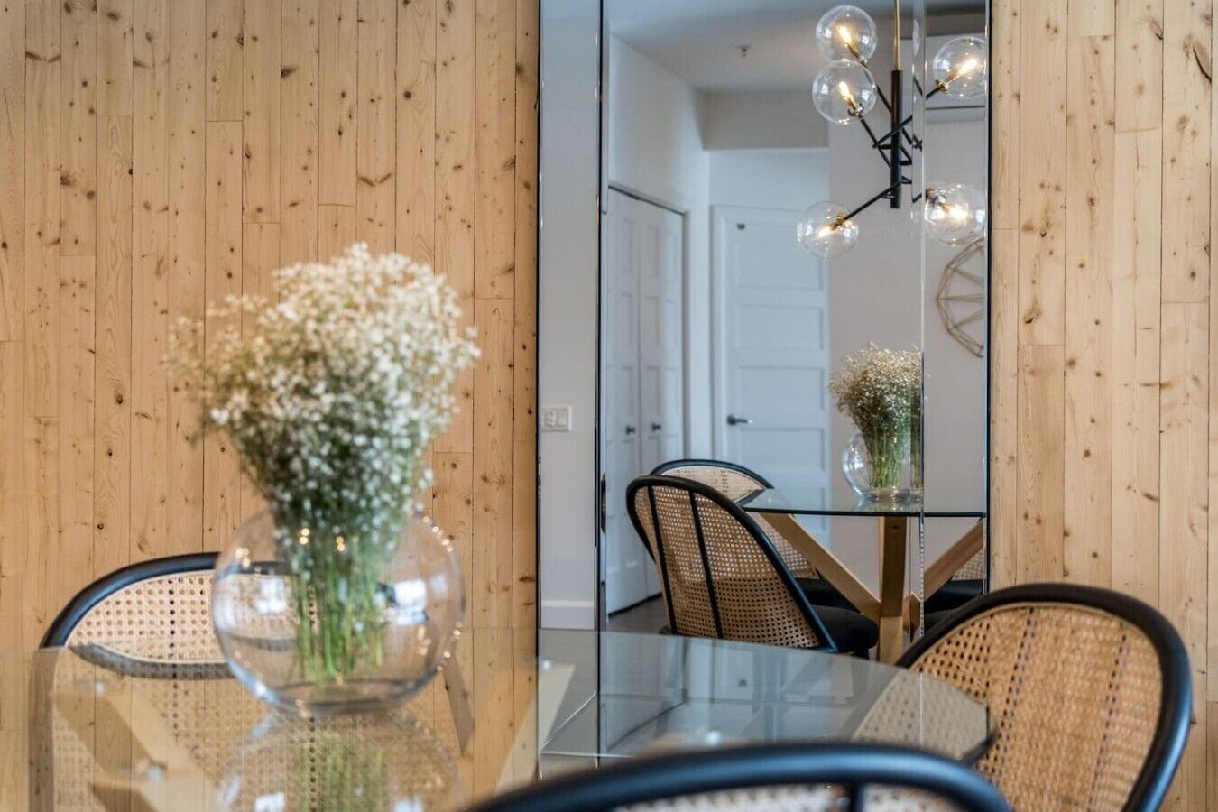 A dining area with a glass table, wicker chairs, and a vase with flowers.