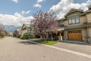 A residential street with houses, a driveway, and a mountain backdrop. - Big Sky Escape: Modern 3 BR Condo / Walk to Town - Minutes to Skiing (Big Sky)