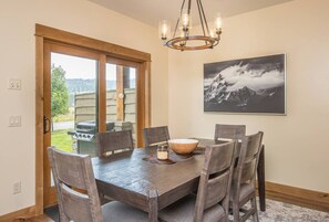 Un coin repas avec une table et des chaises en bois, un lustre et un tableau représentant un paysage de montagne accroché au mur.