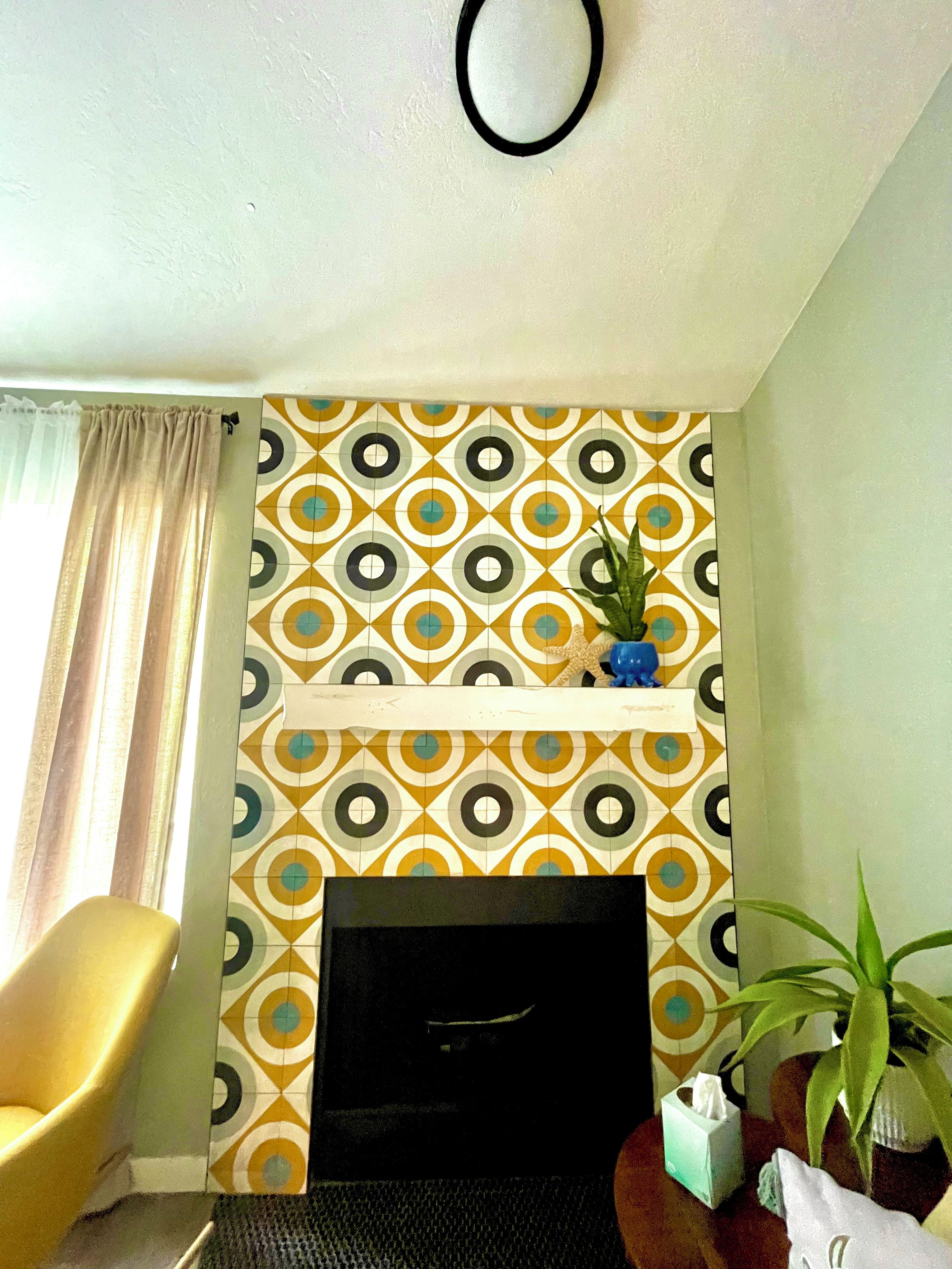 Ein Wohnzimmer mit einer Wand mit Muster, einem Kamin, einem gelben Sessel und einer Topfpflanze.