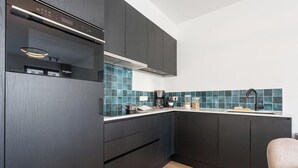 A modern kitchen with dark cabinetry, a built-in microwave, and a backsplash of blue tiles. - DuinGeluk - cosy stay near the sea & marina (Nieuwpoort)