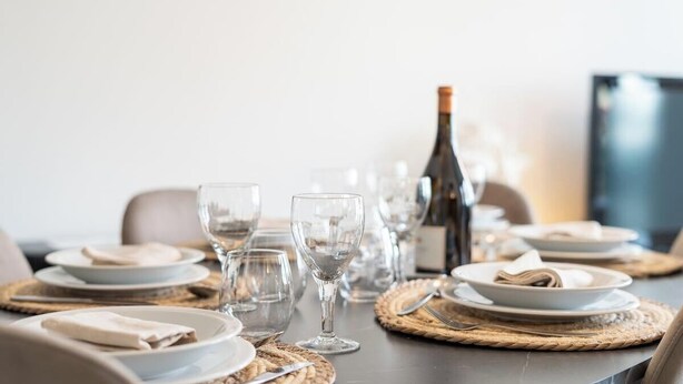 A dining table set with plates, glasses, and a bottle, suggesting a prepared meal setting. - DuinGeluk - cosy stay near the sea & marina (Nieuwpoort)