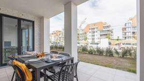 A covered outdoor dining area with a table set for four, surrounded by chairs, and a view of residential buildings in the background. - DuinGeluk - cosy stay near the sea & marina (Nieuwpoort)