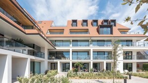 A modern multi-story building with a flat roof, large windows, and a courtyard with outdoor seating. - DuinGeluk - cosy stay near the sea & marina (Nieuwpoort)