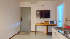 Cozinha compacta com micro-ondas, pia e televisão presa na parede.