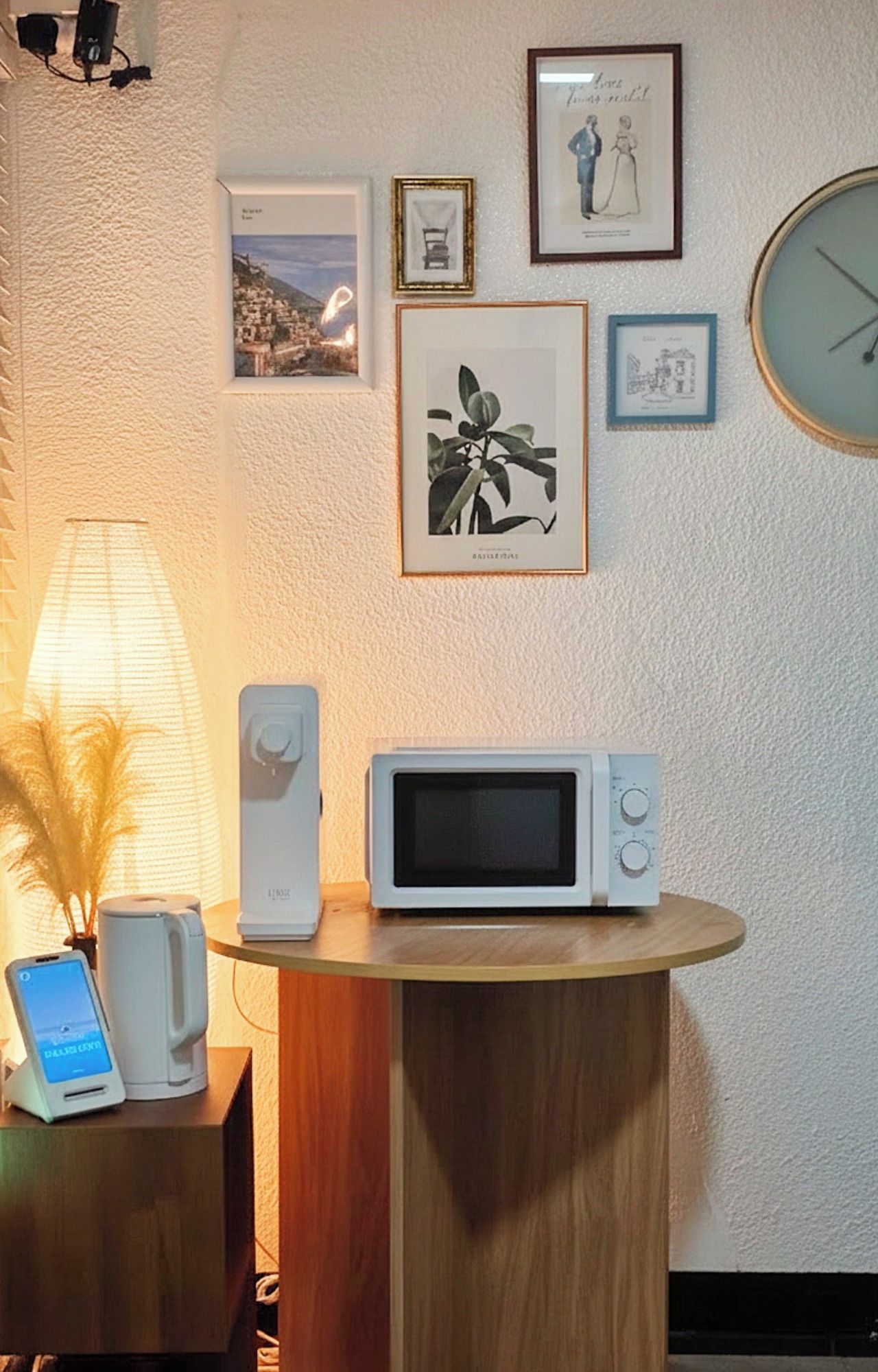A room with a wooden table, a white microwave, a smartphone, and a lamp.
