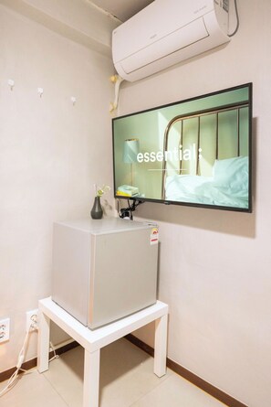 Una habitación con una cama, un televisor montado en la pared y un armario blanco.