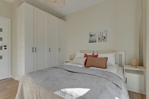 A bedroom with a bed, white wardrobe, artwork on the wall, and a bedside table. - Slow Seaside Brzeźno by Lion Apartments (Gdańsk)