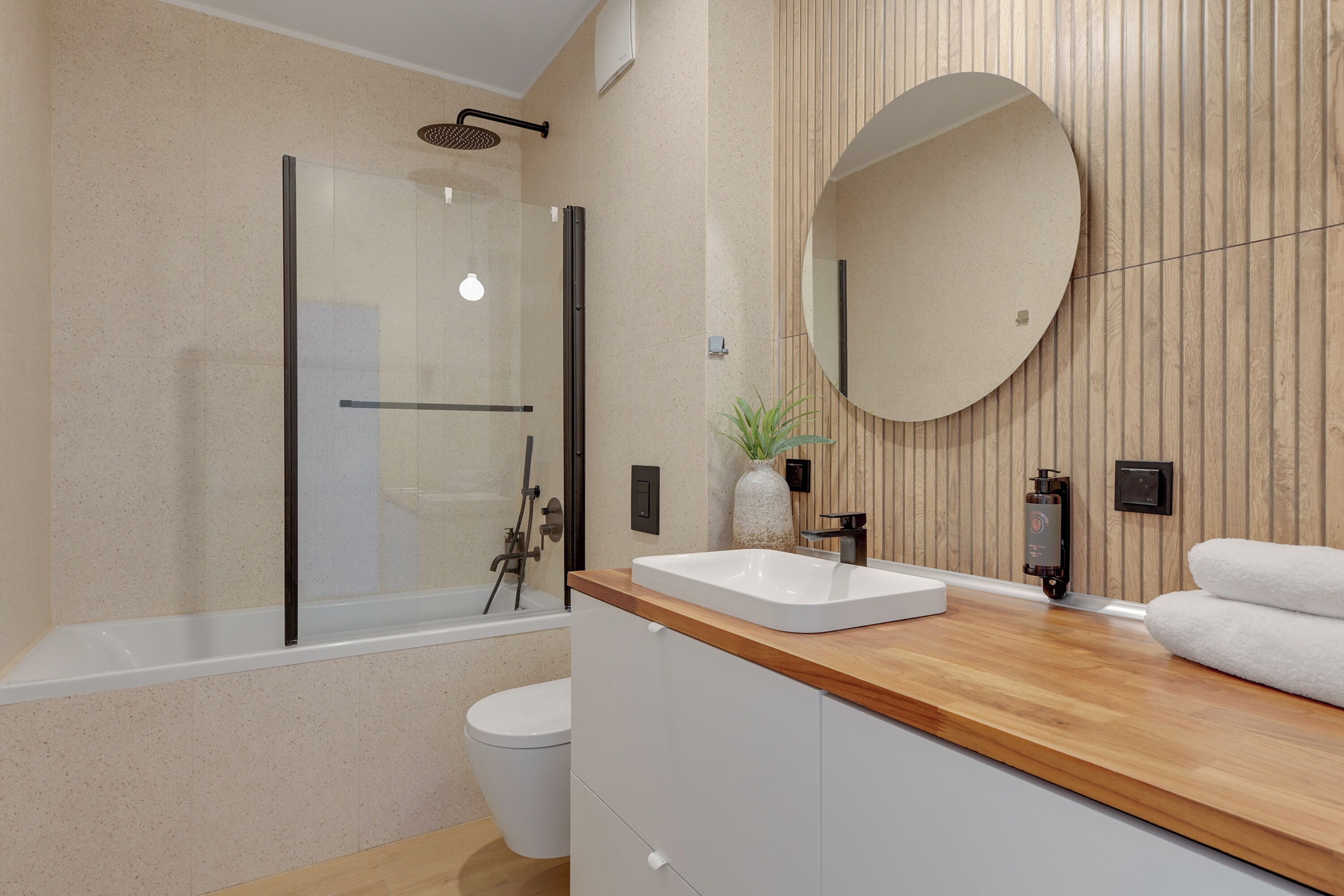 Un baño moderno con ducha de vidrio, tocador de madera con un espejo grande y un inodoro blanco.