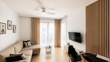 A modern living room with a sofa, a dining table, and a flat-screen TV mounted on the wall.