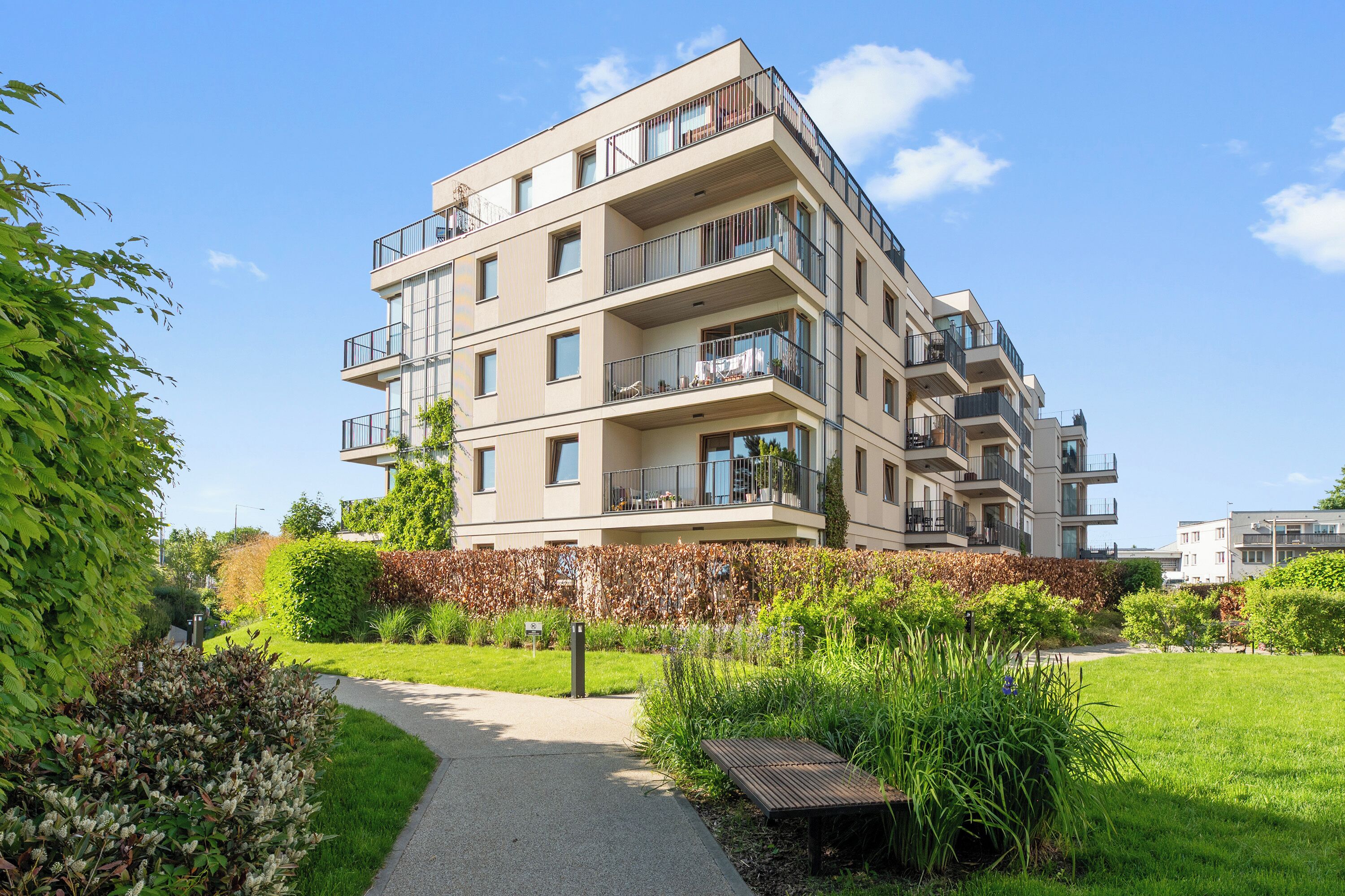 A multi-story residential building with balconies, a paved pathway, and surrounding greenery.