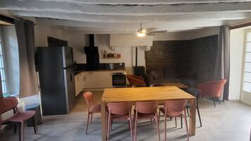 A spacious dining area with a wooden table and chairs, a kitchen in the background, and a ceiling with exposed beams.