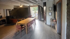 A spacious room with a wooden dining table, chairs, a sofa, and a television.