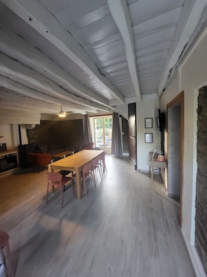 A spacious room with a wooden dining table, chairs, a sofa, and a television.