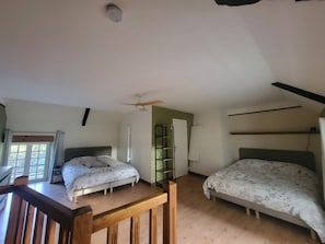 A bedroom with two beds, a ceiling fan, and a window.