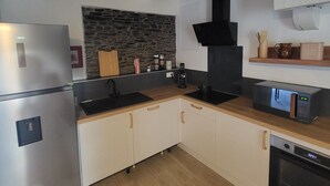 A modern kitchen with a stainless steel refrigerator, a stone backsplash, wooden cabinets, and a black range hood.