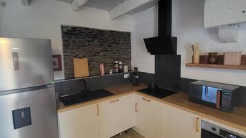 A modern kitchen with a stainless steel refrigerator, a stone backsplash, wooden cabinets, and a black range hood.