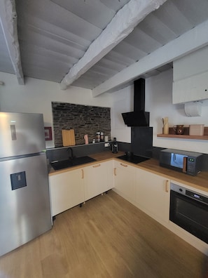 A modern kitchen with a stainless steel refrigerator, a stone backsplash, wooden cabinets, and a black range hood.