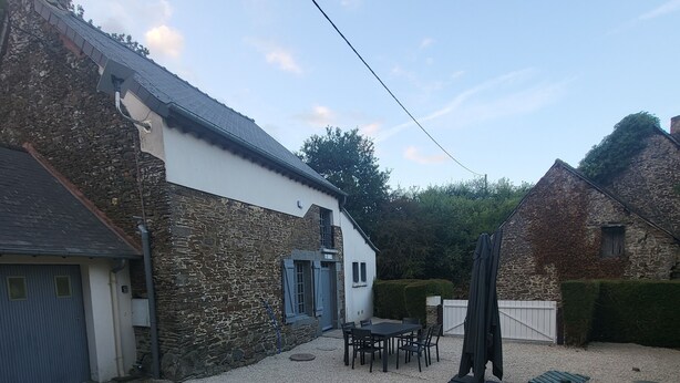A gravel courtyard with a stone building, a table with chairs, and a covered area.