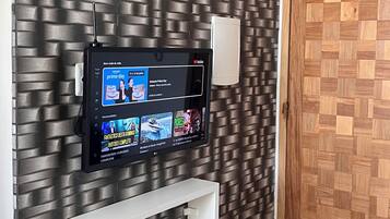 A modern interior with a flat-screen TV mounted on a textured wall, white shelving units, and a wooden door.