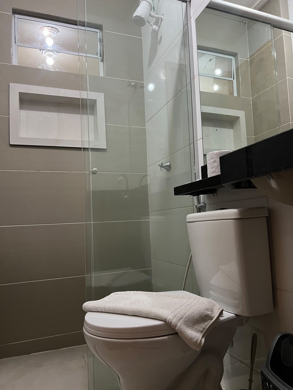 Un baño con inodoro, cabina de ducha de vidrio y espejo sobre el lavabo.