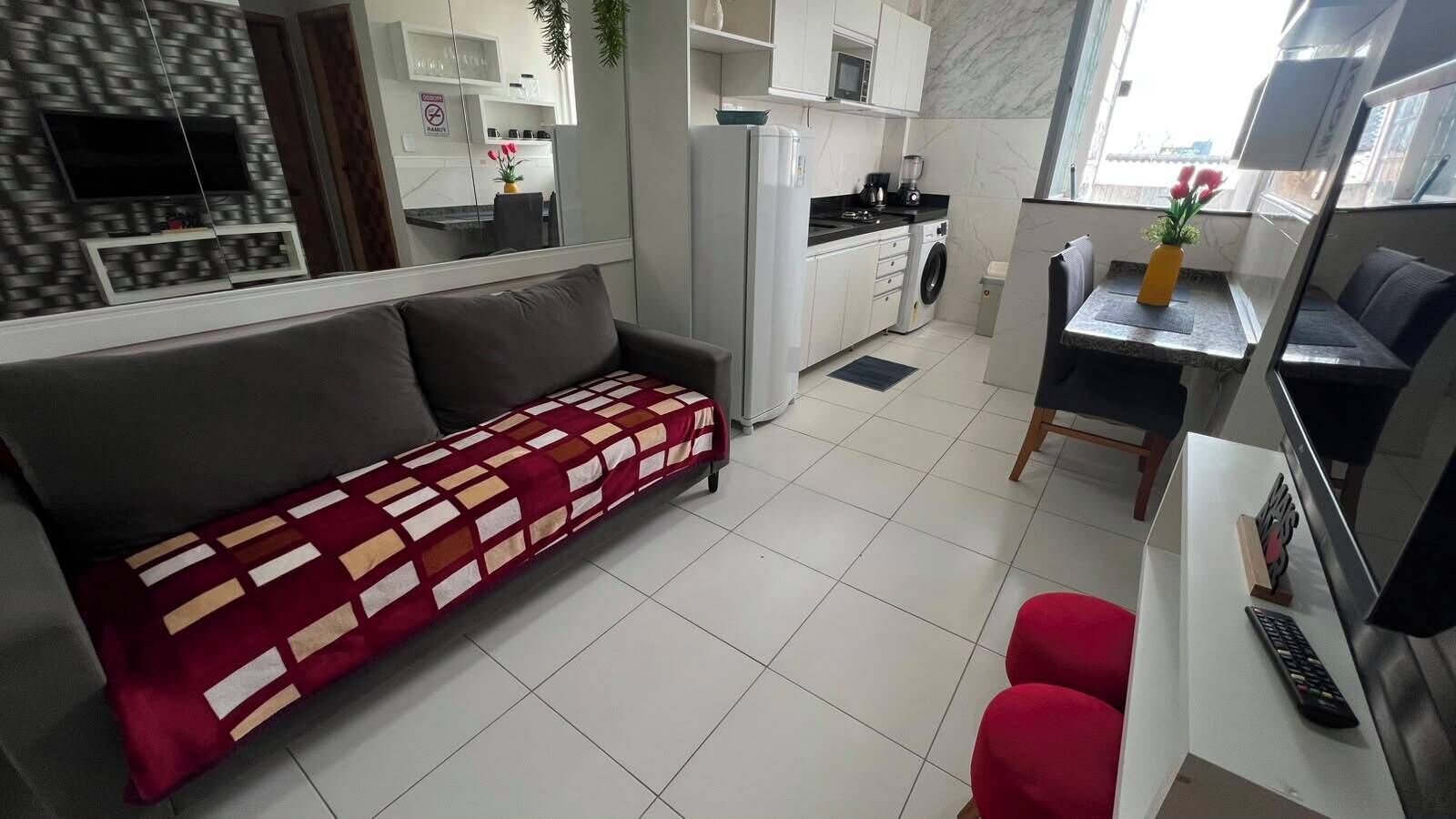 A modern living room with a sofa, a dining area with a table and chairs, a kitchen with appliances, and a TV.