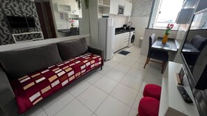 A modern living room with a sofa, a dining area with a table and chairs, a kitchen with appliances, and a TV. - Apto 303 2 Qtos 15 min do Centro (Belém)