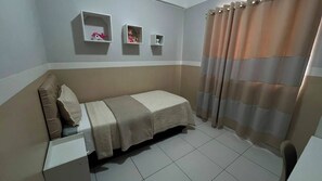 A small, single-bed room with a bed, a nightstand, and a shelf with decorative items. - Apto 303 2 Qtos 15 min do Centro (Belém)