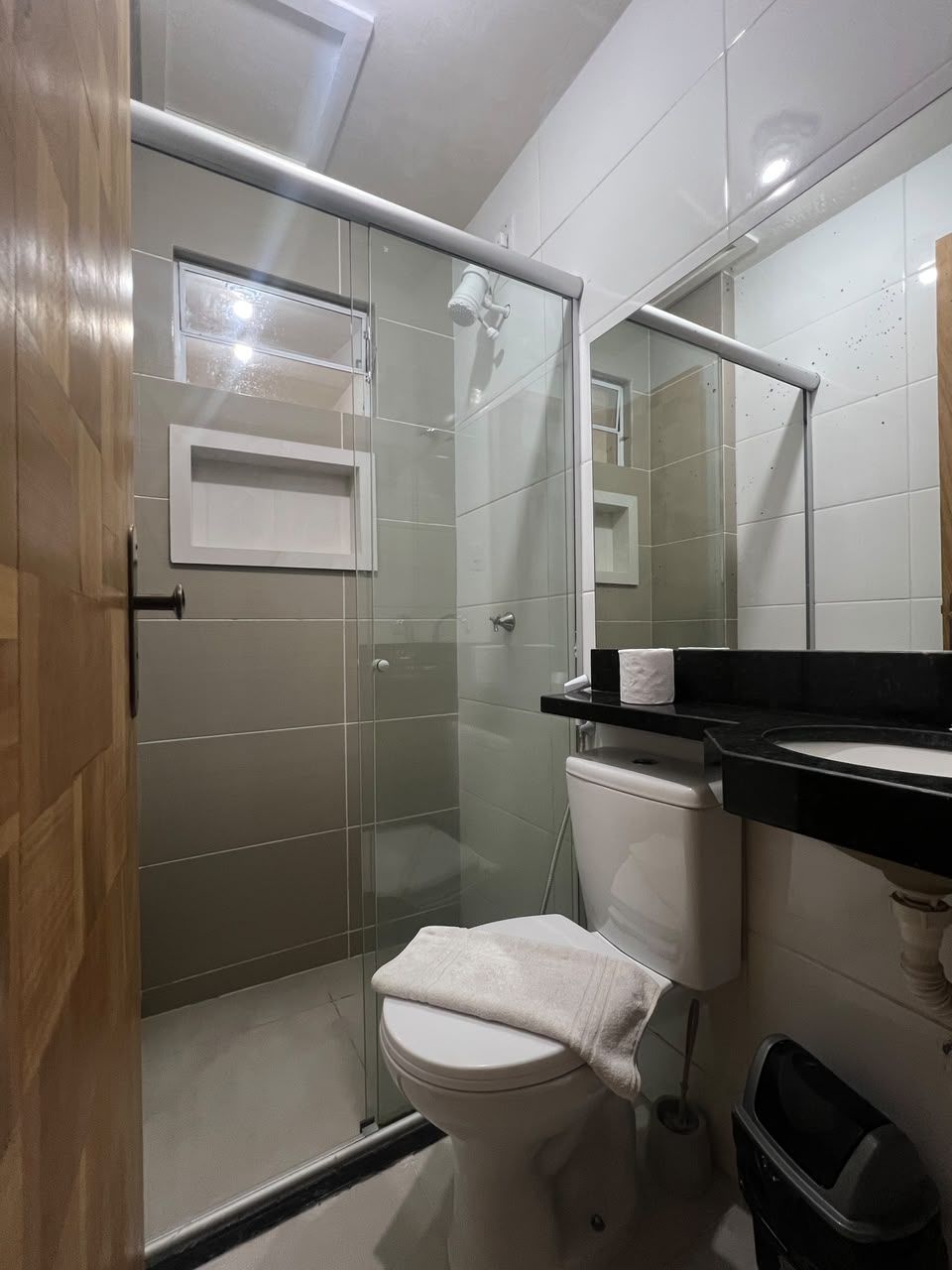 A bathroom with a glass shower enclosure, a toilet, a sink with a black countertop, and a mirror.
