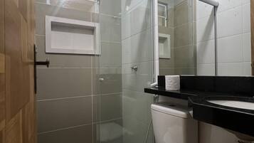 A bathroom with a glass shower enclosure, a toilet, a sink with a black countertop, and a mirror.