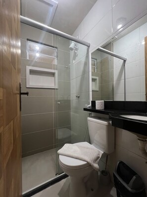 A bathroom with a glass shower enclosure, a toilet, a sink with a black countertop, and a mirror. - Apto 303 2 Qtos 15 min do Centro (Belém)