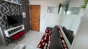 A modern living room with a flat-screen TV, a sofa, red chairs, a patterned rug, and a wooden door. - Apto 303 2 Qtos 15 min do Centro (Belém)